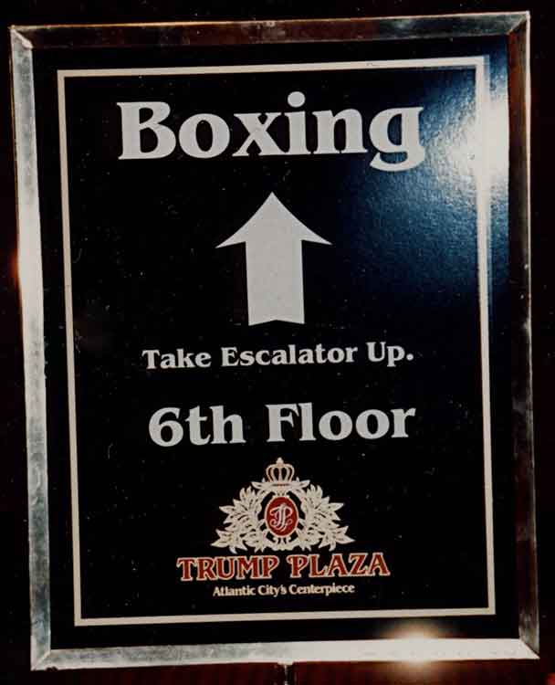 a sign in a stanchion that reads 'Boxing, Take Escalator Up. 6th Floor' with the Trump Plaza logo